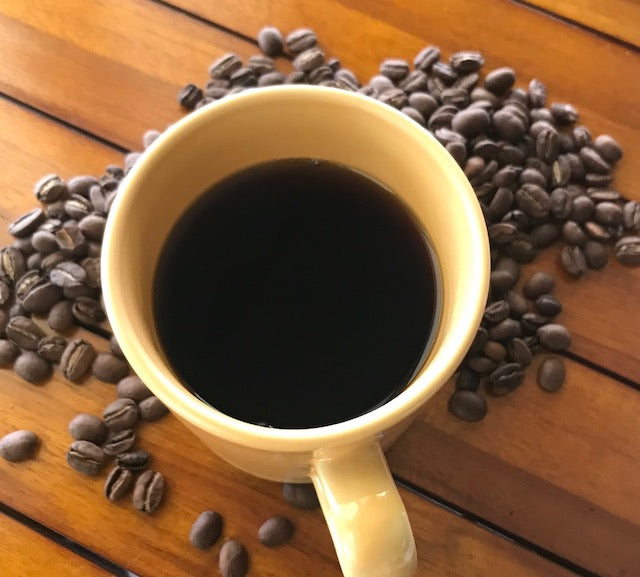 coffee mug filled with brewed coffee in middle of roasted coffee beans